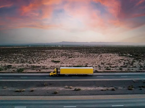 Aerial drone shot of a yellow semi truck on the highway with a vibrant colored sunset near el paso, texas